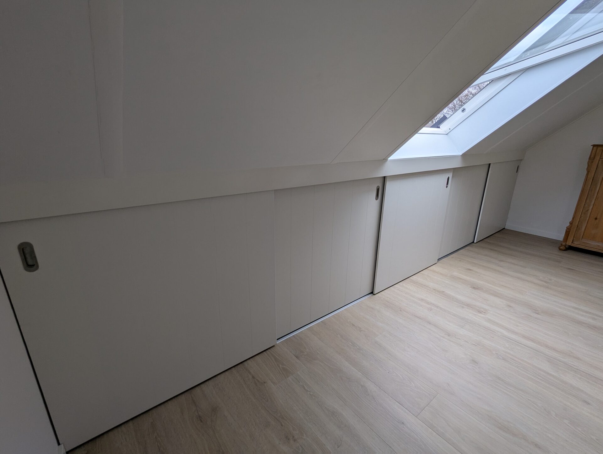 Maatwerk schuine wand met schuifdeuren op zolder, ontworpen voor optimale ruimtebenutting en een strak, modern interieur